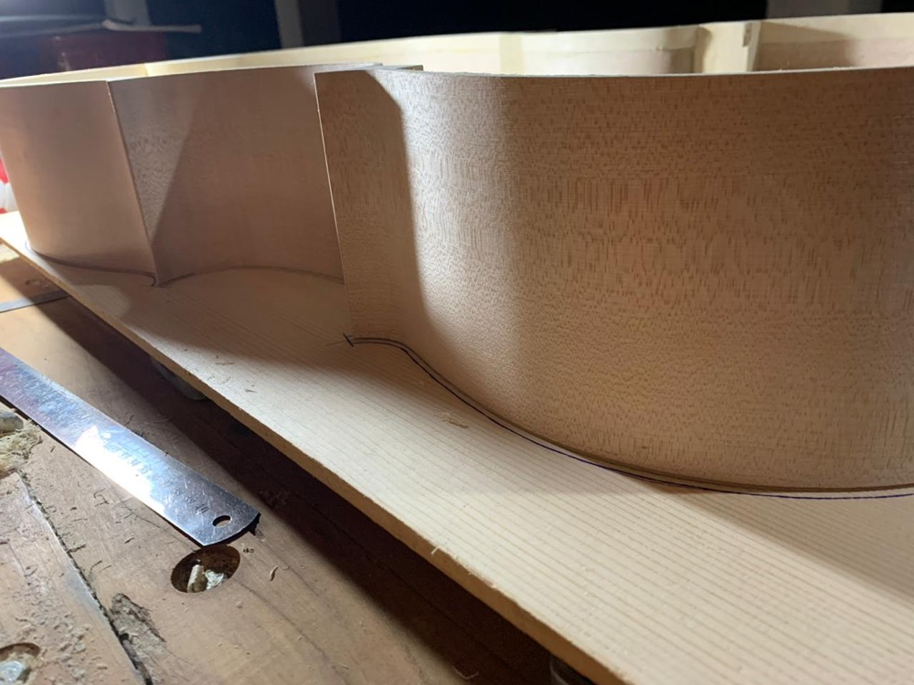 Peças de madeira curvadas sobre tampo traçado a lápis, com régua na bancada.