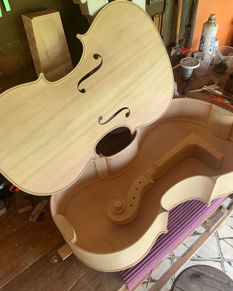 Tampo com furos em f e corpo de violoncelo em montagem sobre bancada de luthier.
