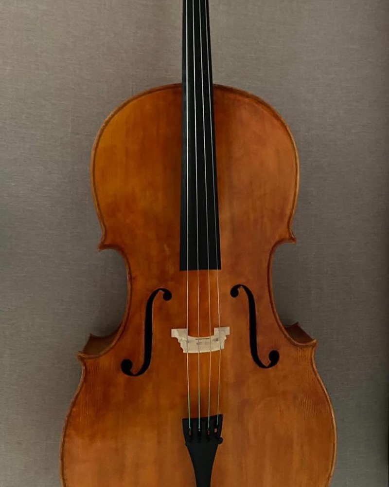 Violoncelo apoiado na bancada entre ferramentas de luthier.