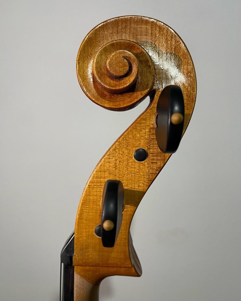 Violoncelo completo apoiado com arco ao lado na bancada.